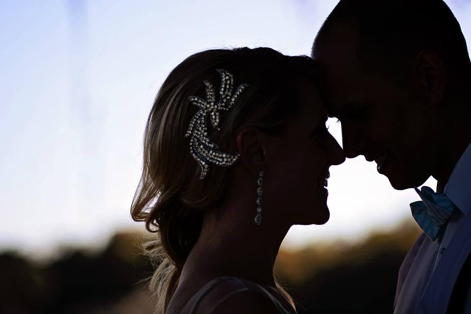 A silhouette profile photo of a bride and groom coming in for a kiss, the glint of the bride's crystal hair piece shining through the dark.