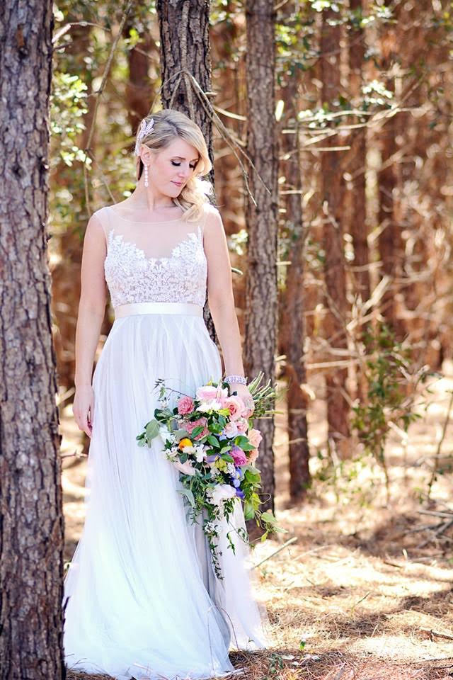 A bride looks down towards her bridal bouquet clutched in her hands as she stands in a grove of winter pines.