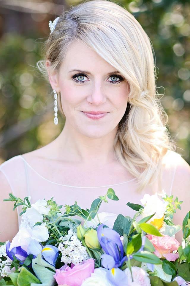 A close-up shot of a lovely blonde bride looking over her colorful bridal bouquet, her long diamond earrings dangling over her shoulder.