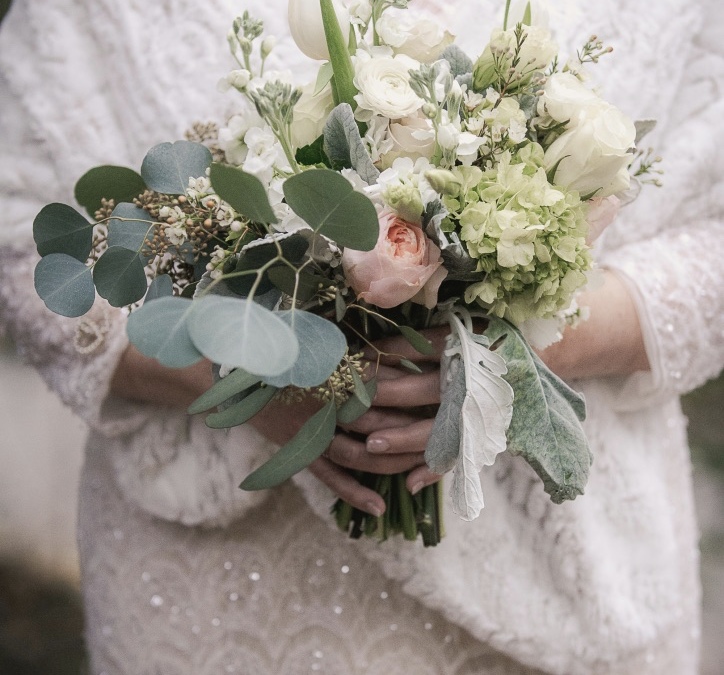A winter bride wearing fur and sequins holds a soft bouquet of eucalyptus and roses.